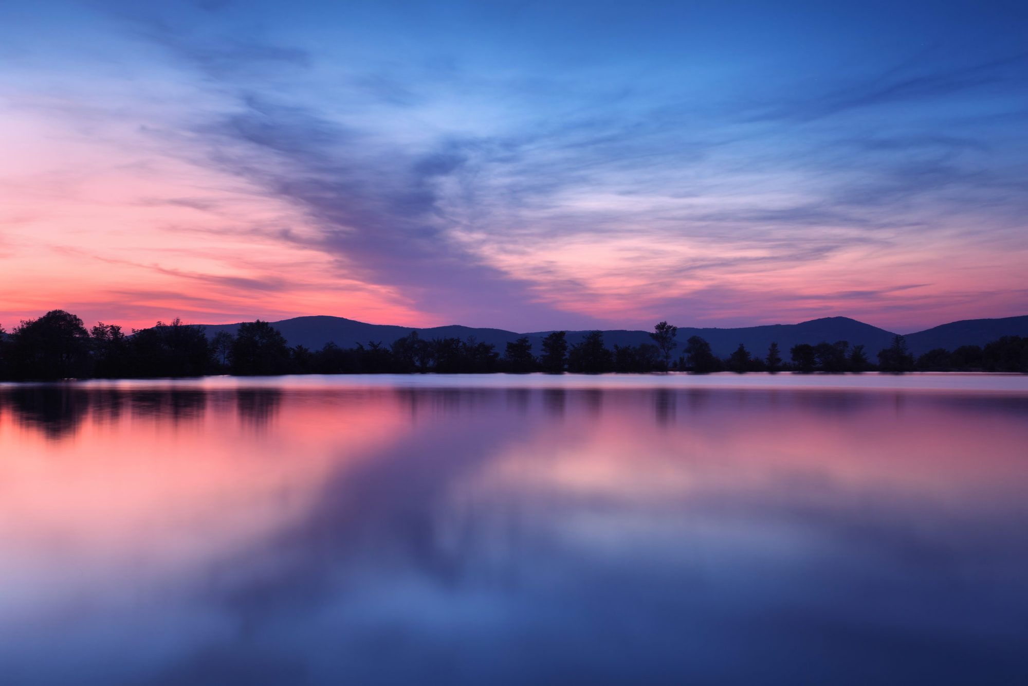 Bergsee in der Abenddämmerung, rosa Himmel spiegelt sich im ruhigen Wasser